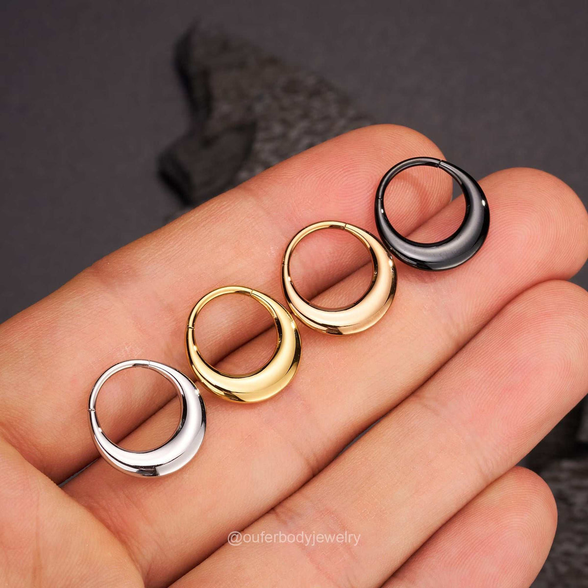 Three crescent-shaped hoop earrings in silver, gold, and black held in a hand.